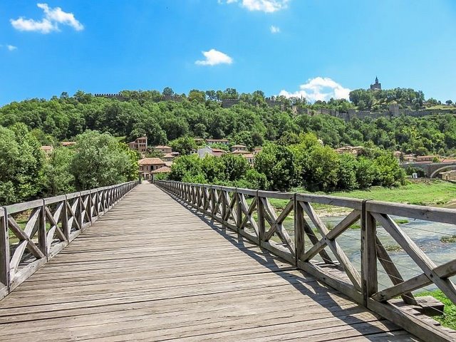 нем, Епископский мост в Велико Тырново, Болгария деревянный мост над рекой, ведущий к зеленому холму с крепостью на нем, Епископский мост в Велико Тырново, Болгария