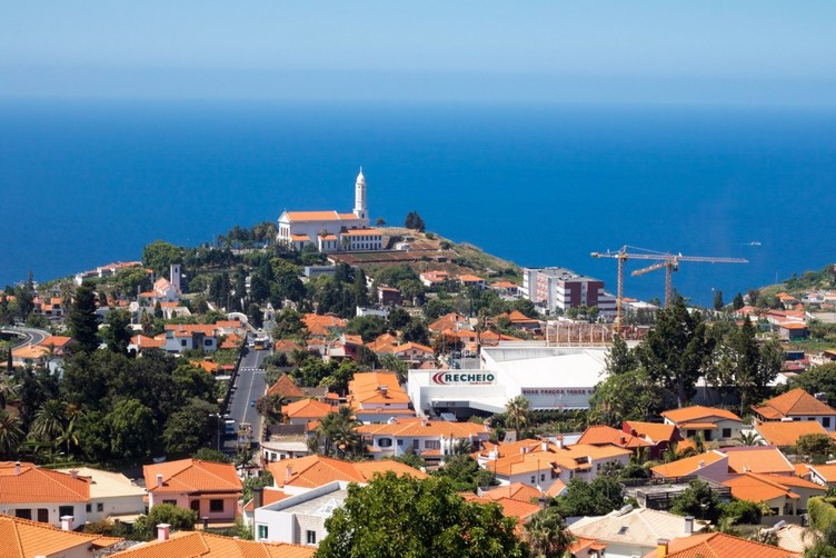 вид из пико-дос-барселуш с точки зрения вида через здания с оранжевой крышей и церковь в городе с океаном на заднем плане-мадейра-маршрут-7 дней 1 вид из пико-дос-барселуш с точки зрения вида через здания с оранжевой крышей и церковь в городе с океаном на заднем плане-мадейра-маршрут-7 дней