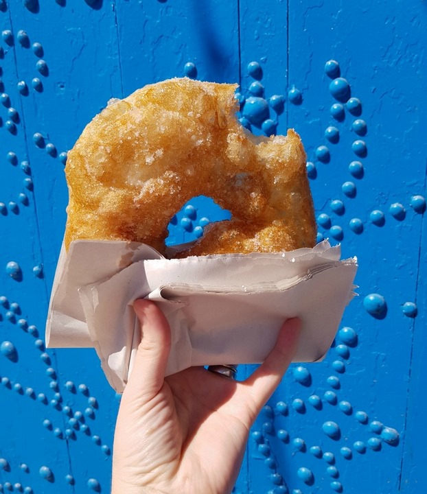 Рука держит амбалуни у синей двери с заклепками - жареная во фритюре выпечка - уже достаточная причина, чтобы посетить Тунис. 1 Рука держит амбалуни у синей двери с заклепками - жареная во фритюре выпечка - уже достаточная причина, чтобы посетить Тунис.